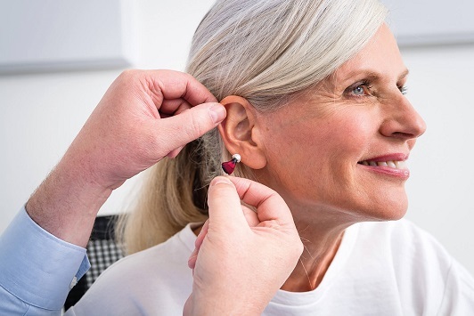 Ältere Frau bekommt ein modernes Hörgerät angepasst, Hörakustiker hilft beim Einsetzen.